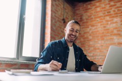 selective focus of happy businessman writing in notebook near laptop in office